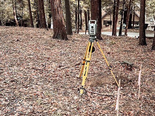 Surveyor using a total station for precise measurement in a wooded area.